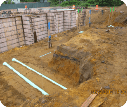 Excavation site with marked underground utilities and retaining wall forms.