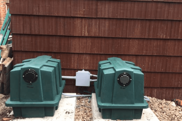 Two green utility boxes mounted on a concrete base against a brown wooden wall, part of IA Systems.