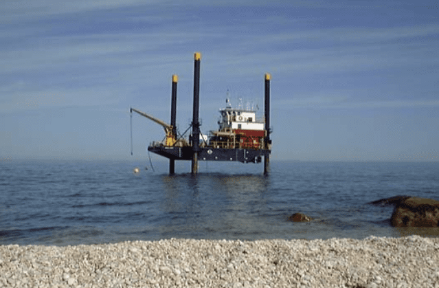Jack-up barge near a pebble shoreline with a clear blue sky, designed for wastewater outfall.