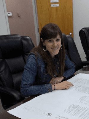 Environmental Scientist in denim shirt smiling at a desk with papers.