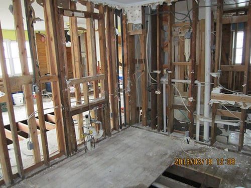 Interior of a house under renovation showing exposed wooden studs and plumbing, with Holzmacher Engineering overseeing the project.
