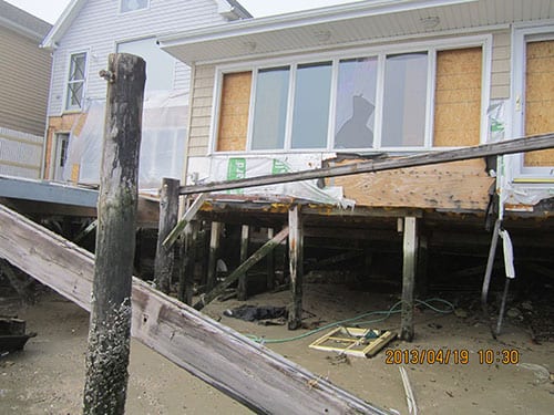 Damaged house with missing walls and debris, showing aftermath of a disaster, now under assessment by Holzmacher Engineering.